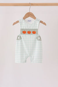 Sage green gingham romper with three orange pumpkin embroidered details on the chest, hanging on a wooden hanger.