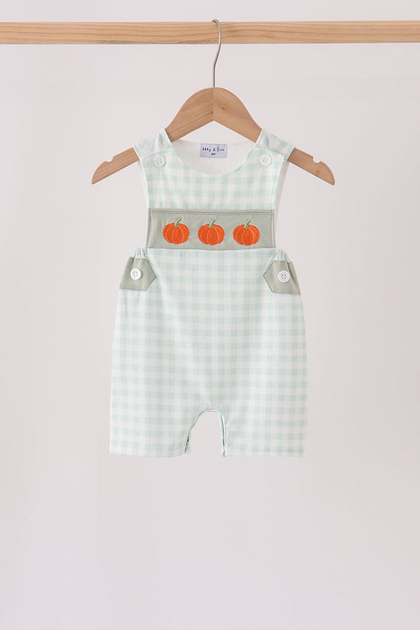 Sage green gingham romper with three orange pumpkin embroidered details on the chest, hanging on a wooden hanger.