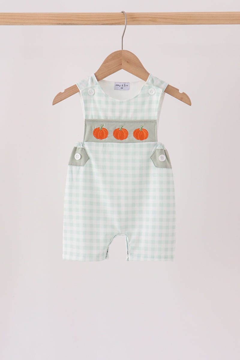 Sage green gingham romper with three orange pumpkin embroidered details on the chest, hanging on a wooden hanger.