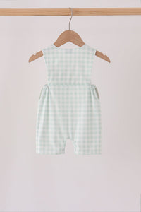 Back view of sage green gingham jon jon romper hanging on a wooden hanger, featuring elastic side gathers and classic checks.