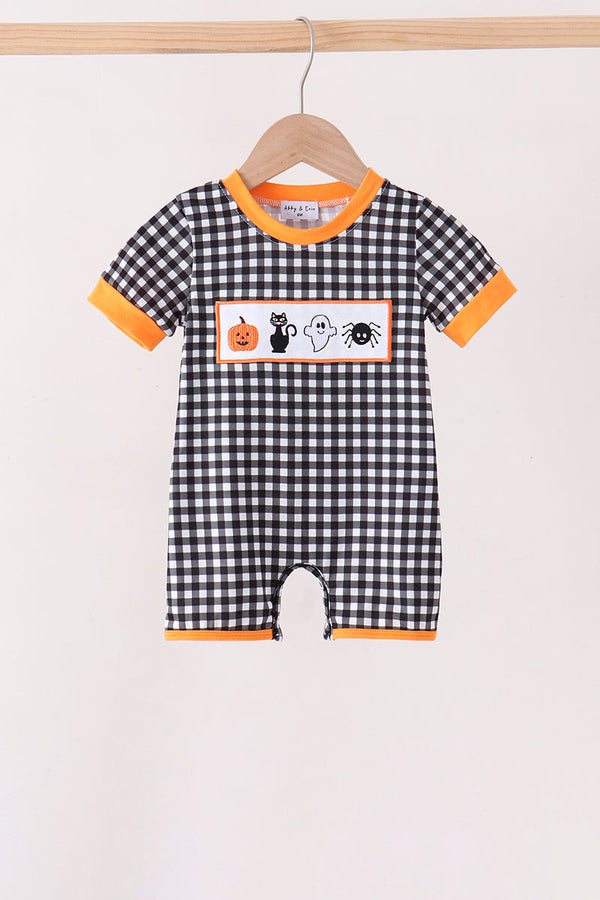 A baby short-sleeve romper with a black and white gingham pattern, orange trim, and a Halloween-themed chest graphic featuring a pumpkin, cat, ghost, and spider, hanging on a wooden hanger.