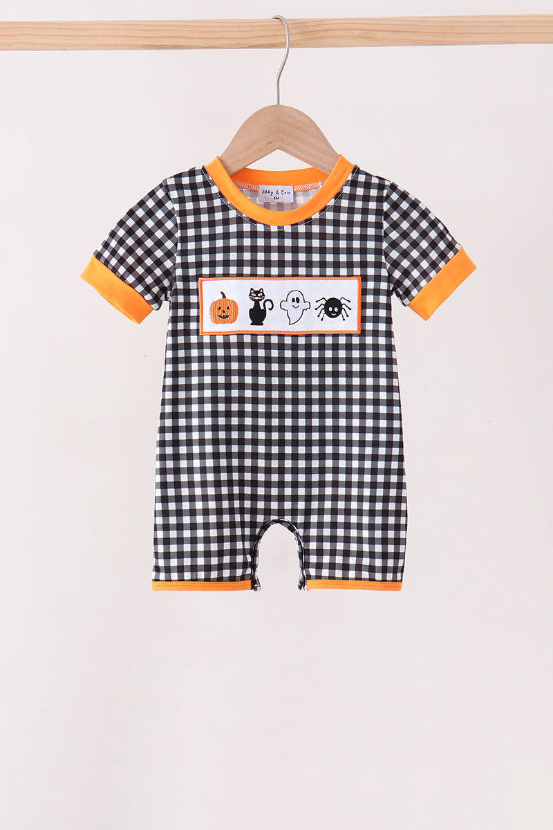 A baby short-sleeve romper with a black and white gingham pattern, orange trim, and a Halloween-themed chest graphic featuring a pumpkin, cat, ghost, and spider, hanging on a wooden hanger.