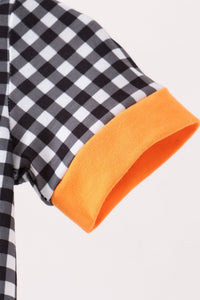 Close-up of a short-sleeve garment showing a black and white gingham pattern on the body and a bright orange ribbed cuff.