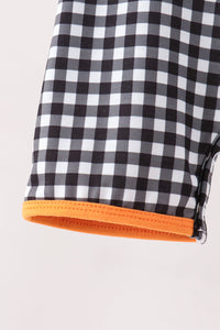 Close-up of a black and white gingham checkered fabric item with a bright orange stitched trim along the edge, shown against a plain light background.