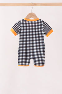 A baby short-sleeve romper with a black and white gingham check pattern and bright orange trim on the collar, cuffs, and leg openings, hanging on a wooden hanger from a light wood rod.