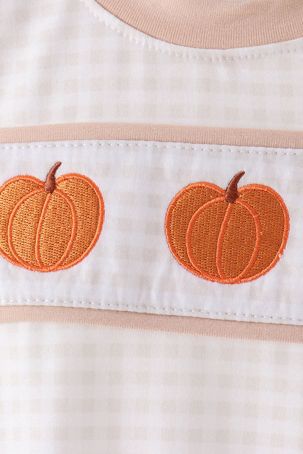 Close-up of orange pumpkin embroidery on beige gingham fabric with tan trim for an autumn bubble outfit.