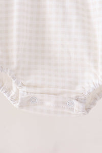 Close-up of cream gingham bubble romper leg with elastic ruching and two white snap buttons for easy dressing.