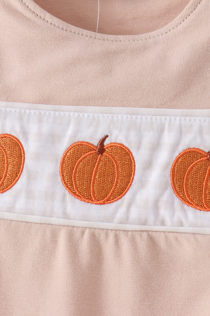 Close-up of a peach-colored garment with a white horizontal band featuring embroidered orange pumpkins.