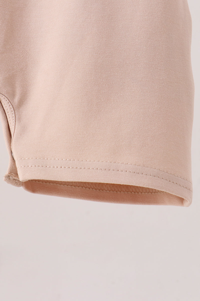 Close-up of a light beige or pale peach knit fabric, showing the texture and hem stitching detail against a plain light background.