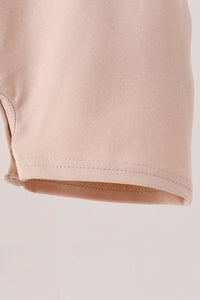 Close-up of a light beige or pale peach knit fabric, showing the texture and hem stitching detail against a plain light background.