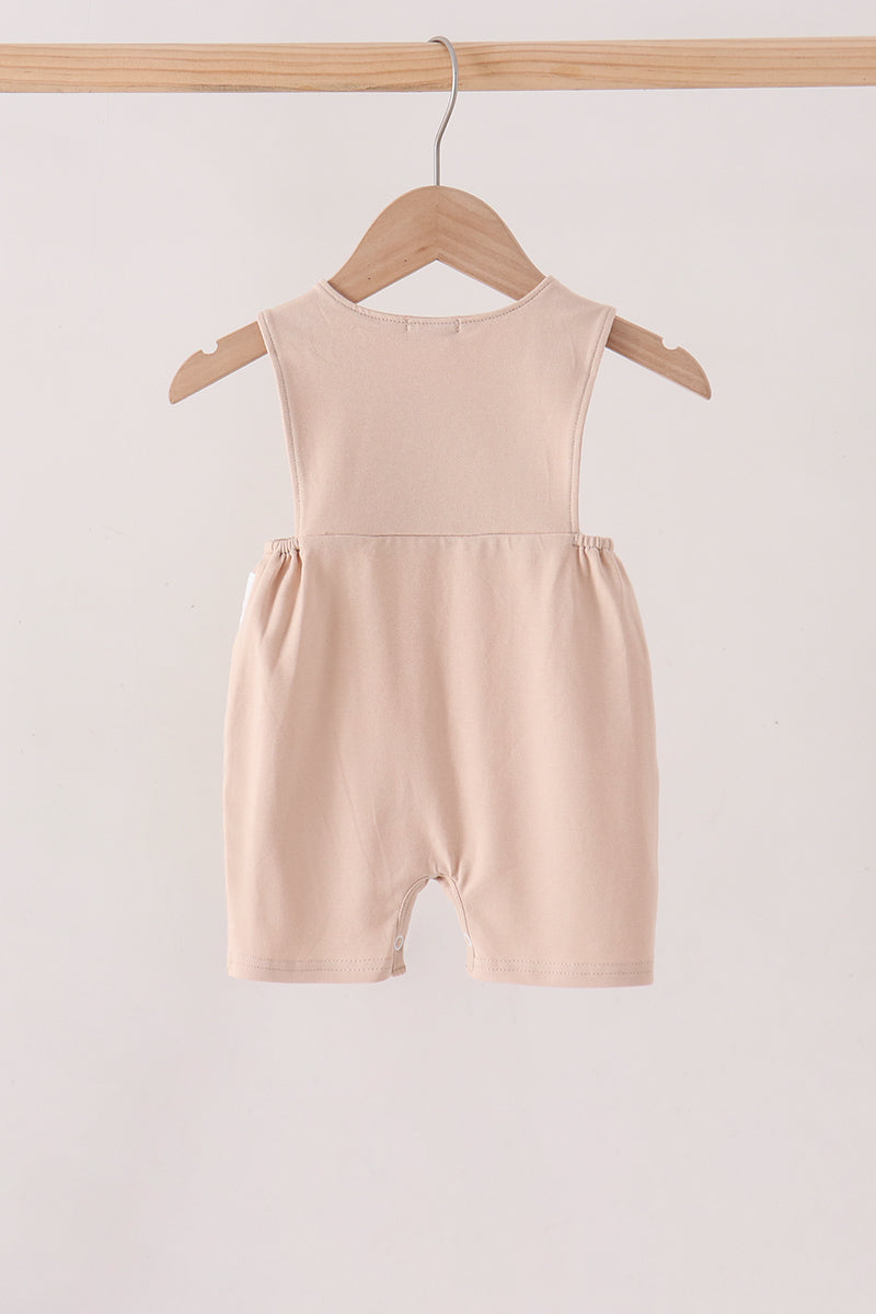 A sleeveless baby romper in a soft blush pink color, hanging on a wooden hanger from a wooden clothing rack against a plain off-white background.
