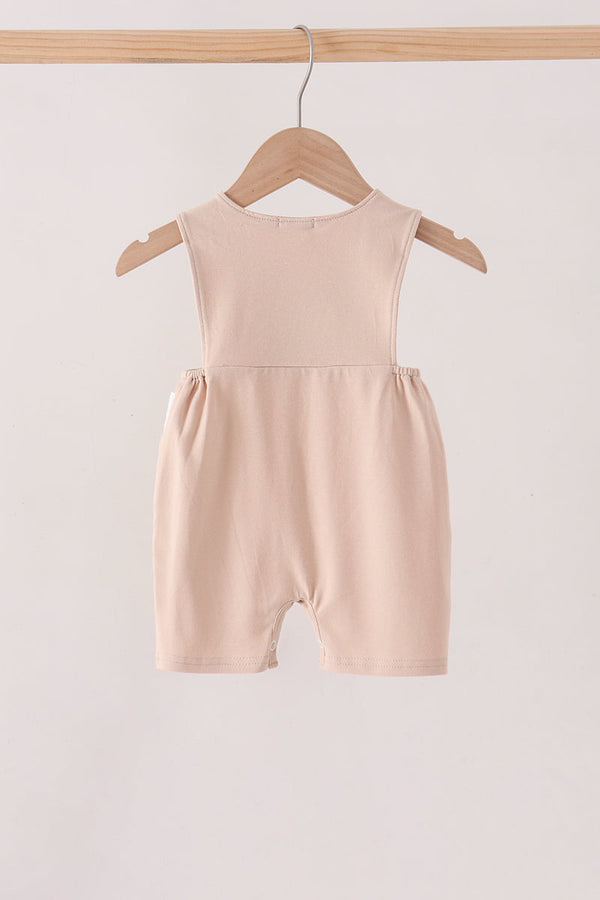 A sleeveless baby romper in a soft blush pink color, hanging on a wooden hanger from a wooden clothing rack against a plain off-white background.
