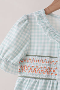 Sage pumpkin smocked gingham dress featuring light blue check pattern, ruffled neckline, and orange embroidery detail on elastic bodice.