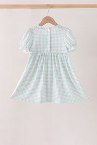 Back view of sage pumpkin smocked gingham dress featuring puff sleeves and white buttons on a wooden hanger.