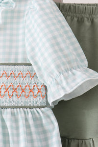 Light green gingham top with orange smocking and ruffled sleeves paired with sage shorts.