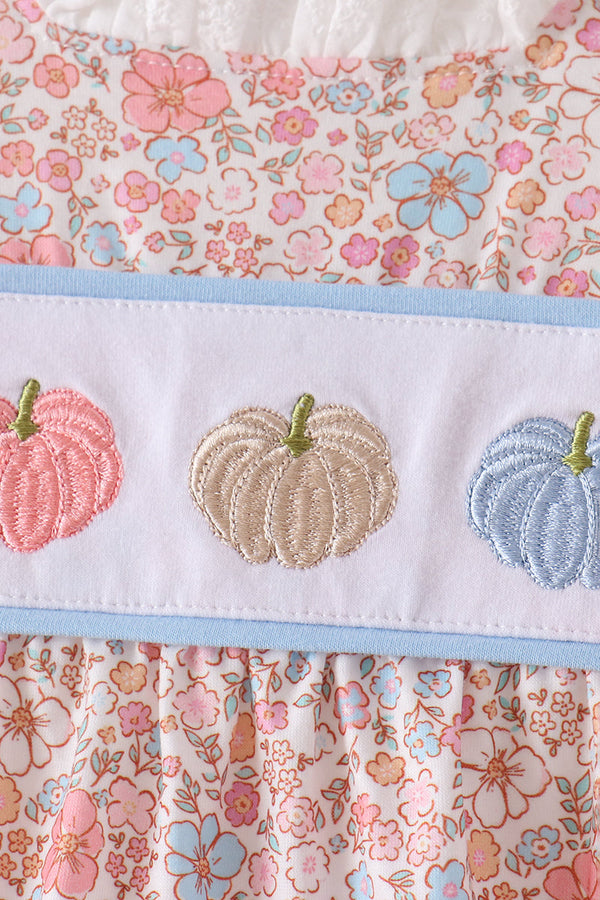 Close-up of embroidered pink, beige, and blue pumpkins on a white band above pastel floral fabric with light blue trim.
