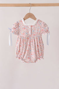 Pink floral bubble onesie with puff sleeves, white lace neckline, front buttons, and blue ribbon ties hanging on a wooden hanger.