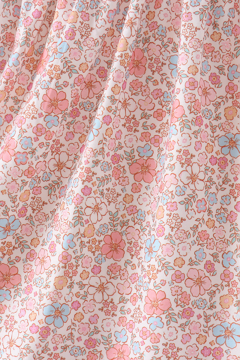 A close-up of a draped fabric with a dense, small-scale floral pattern in pink, light blue, and peach on a warm off-white background.
