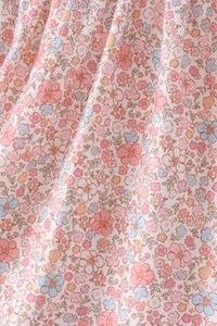 A close-up of a draped fabric with a dense, small-scale floral pattern in pink, light blue, and peach on a warm off-white background.