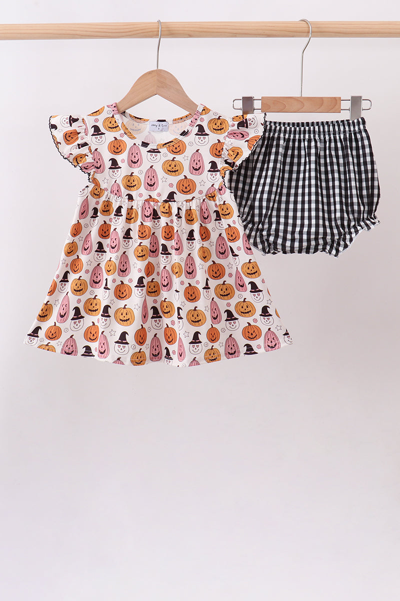 A toddler girl's two-piece Halloween outfit hanging on wooden hangers against a plain light background. The set includes a short-sleeve dress with an all-over pumpkin print and matching black-and-white gingham bloomers.
