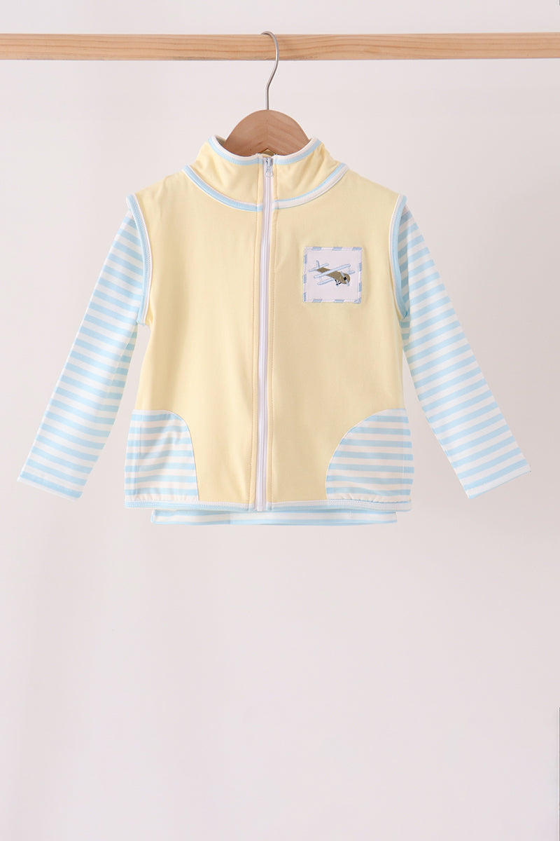 A baby long-sleeve zip-up vest with a pale yellow body and light blue and white striped sleeves, hanging on a wooden hanger against a plain light background.