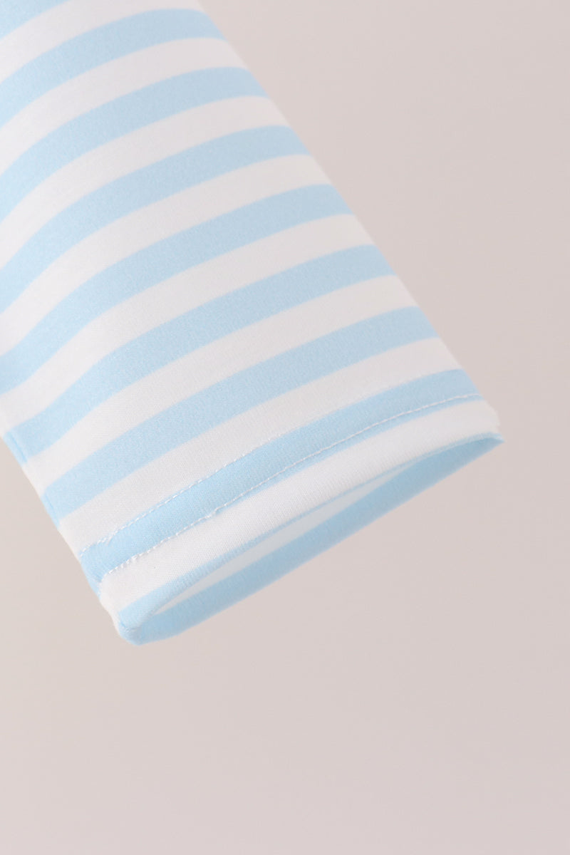 A close-up of a folded fabric item, likely a baby blanket or swaddle, featuring light blue and white horizontal stripes, set against a solid pale pink background.