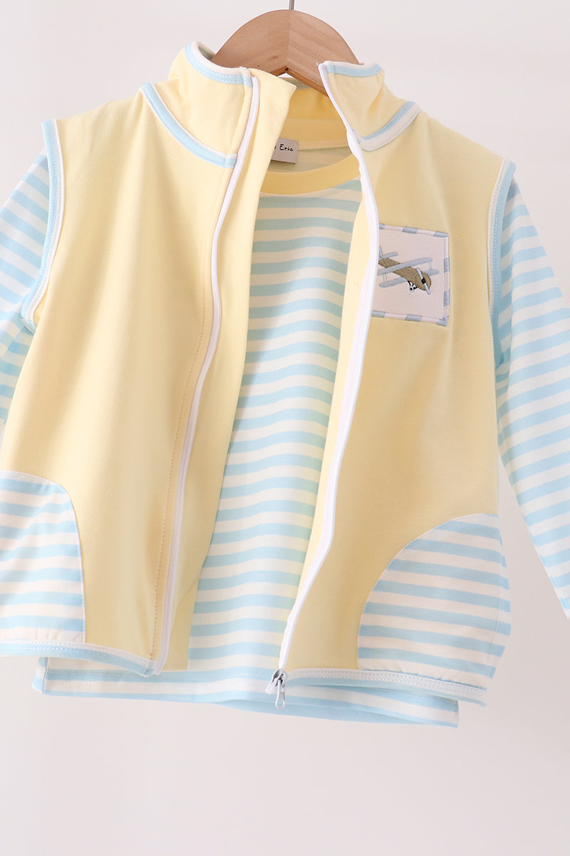 A children's zip-front vest layered over a light blue and white striped long-sleeve shirt, hanging on a wooden hanger against a plain light background.