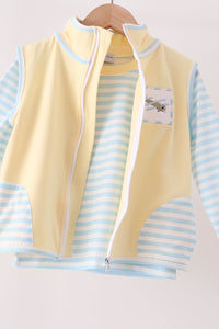 A children's zip-front vest layered over a light blue and white striped long-sleeve shirt, hanging on a wooden hanger against a plain light background.