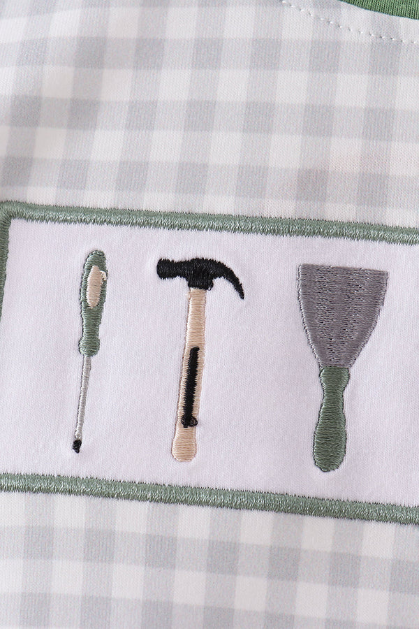 Close-up of a white embroidered patch featuring three hand tools—a screwdriver, a hammer, and a putty knife—embroidered on a gray and white gingham fabric background.