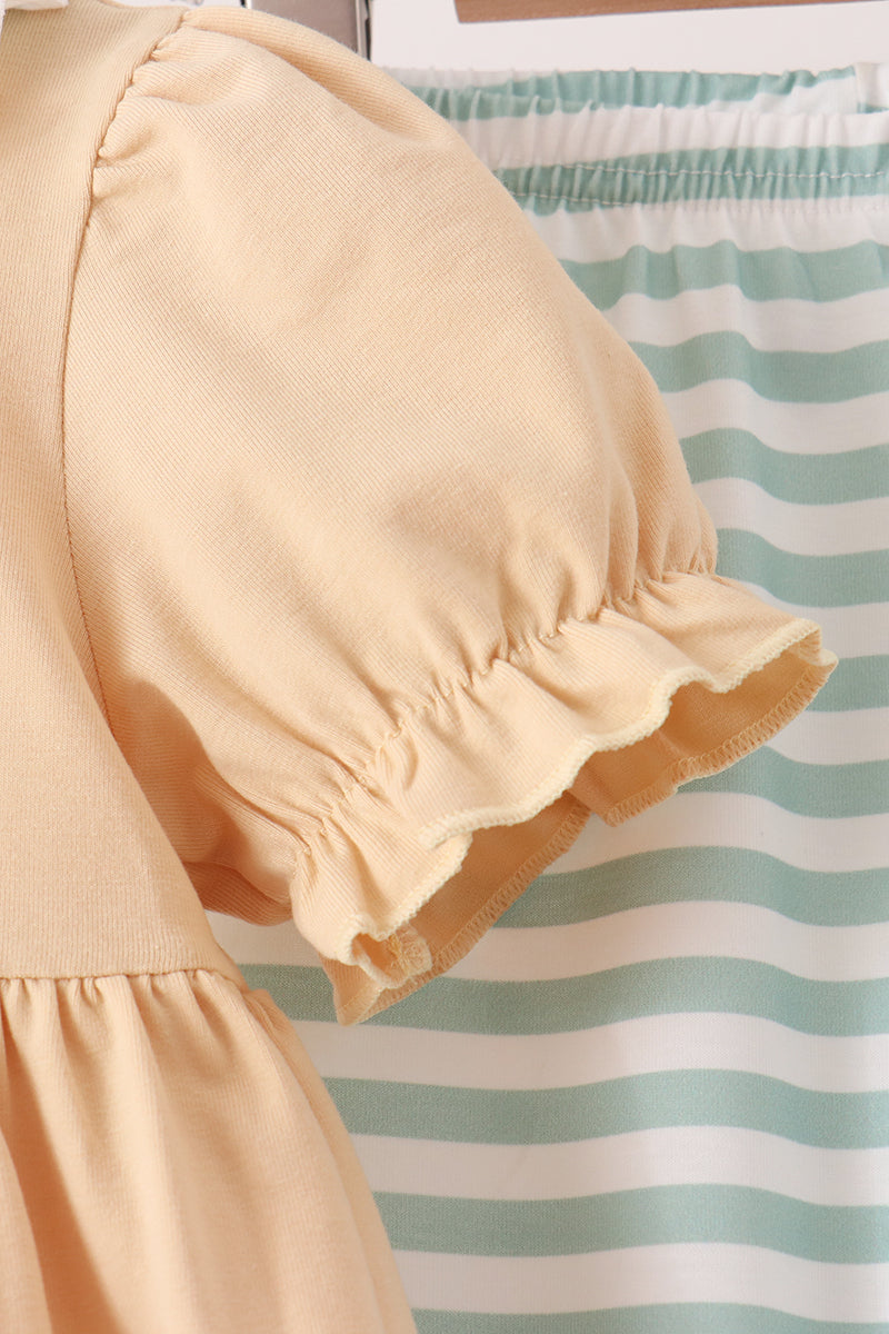 Close-up of a light peach or pale yellow ruffled blouse sleeve with gathered puff detailing, shown against a mint green and white striped fabric background.