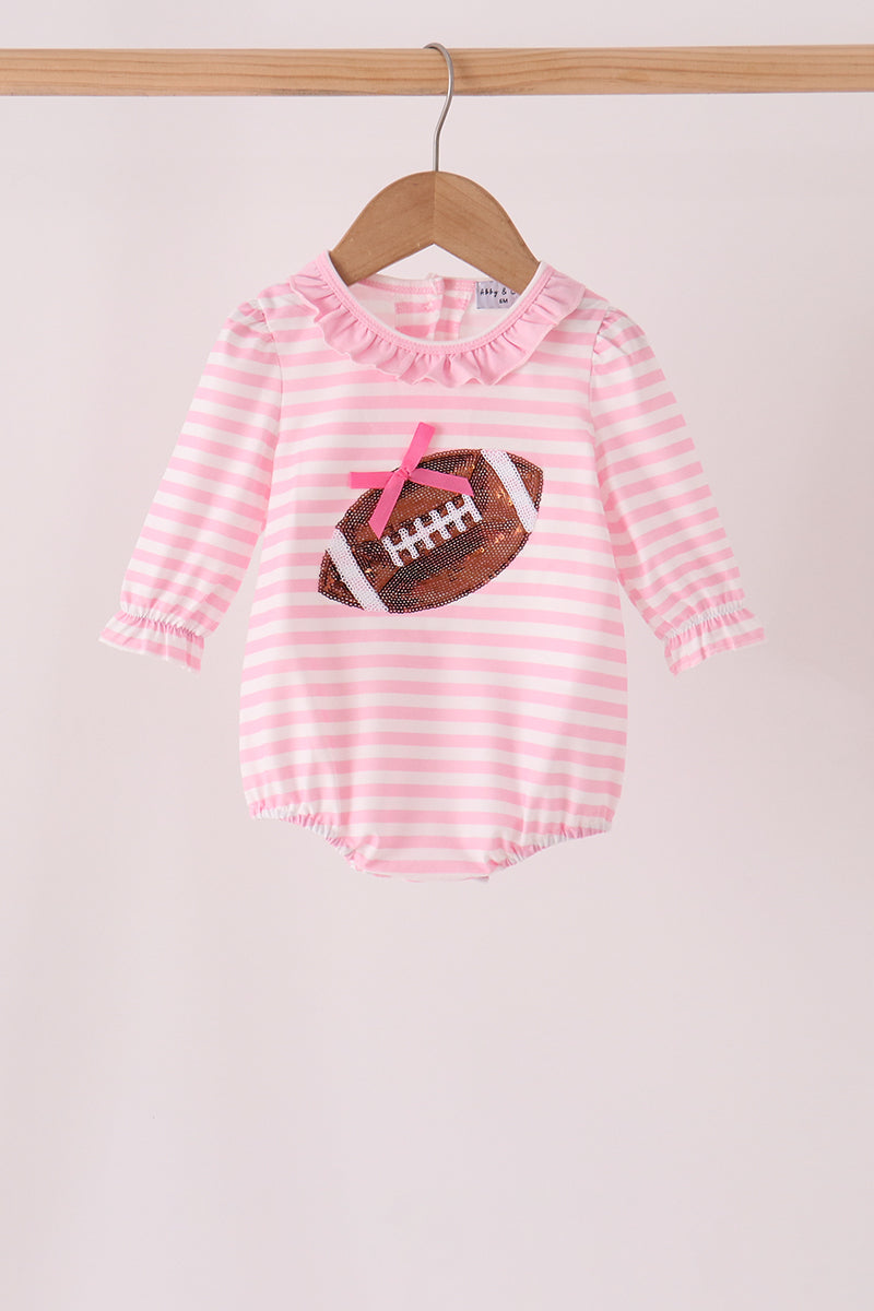 A baby girl's long-sleeve romper with pink and white horizontal stripes, featuring a ruffled collar and a football graphic on the front with a pink bow, hanging on a wooden hanger.