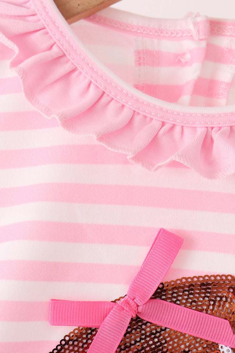 Close-up of a pink and white striped garment with a ruffled neckline and a bright pink ribbon bow, shown on a hanger.