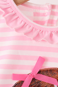 Close-up of a pink and white striped garment with a ruffled neckline and a bright pink ribbon bow, shown on a hanger.