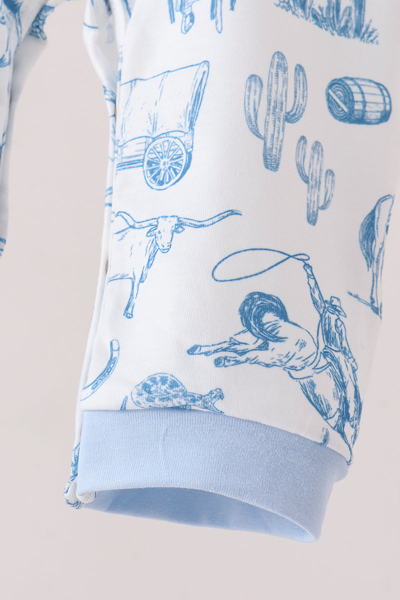 A close-up of a white garment with a blue western-themed print featuring cacti, a longhorn steer, a lasso, and a barrel, finished with a light blue ribbed cuff.