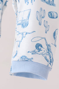 A close-up of a white garment with a blue western-themed print featuring cacti, a longhorn steer, a lasso, and a barrel, finished with a light blue ribbed cuff.