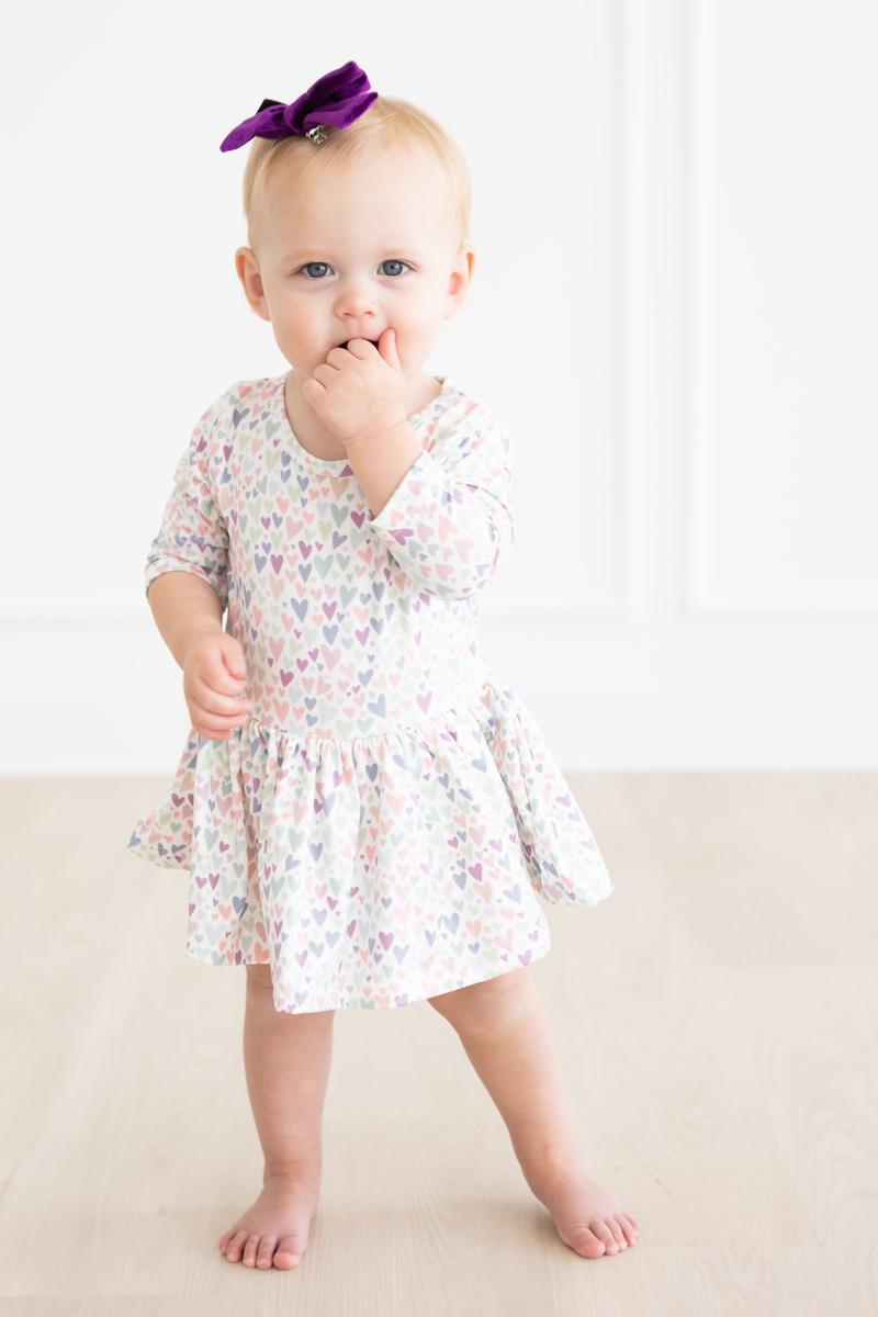 Adorable baby in the One in a Million 3/4 Sleeve Twirl Bodysuit by Mila & Rose®, showcasing a charming heart pattern and ready to twirl.