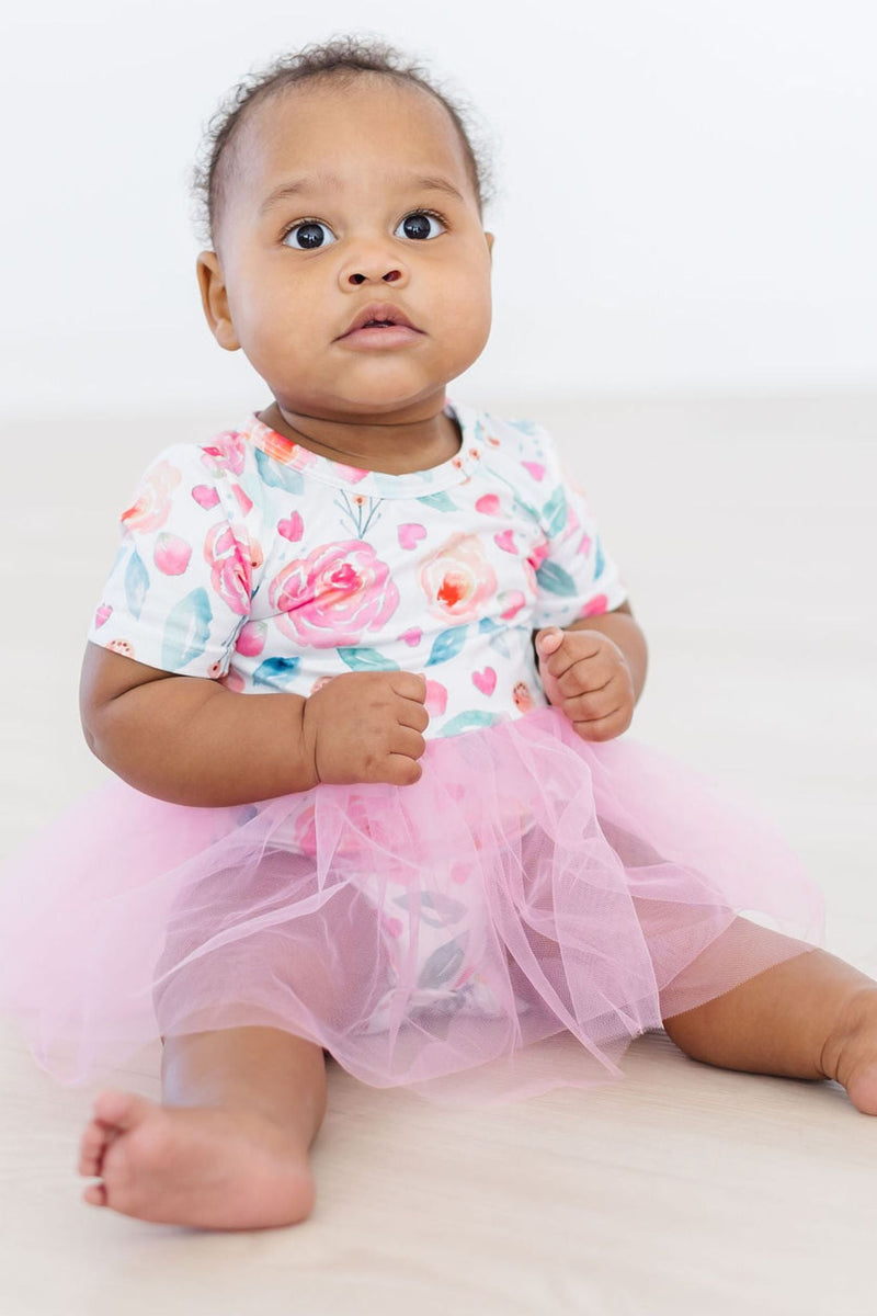 Infant sitting happily in a SALE Rosettes Pink Tutu Bodysuit for Babies and Toddlers, surrounded by playful decor, with a fluffy pink tutu.