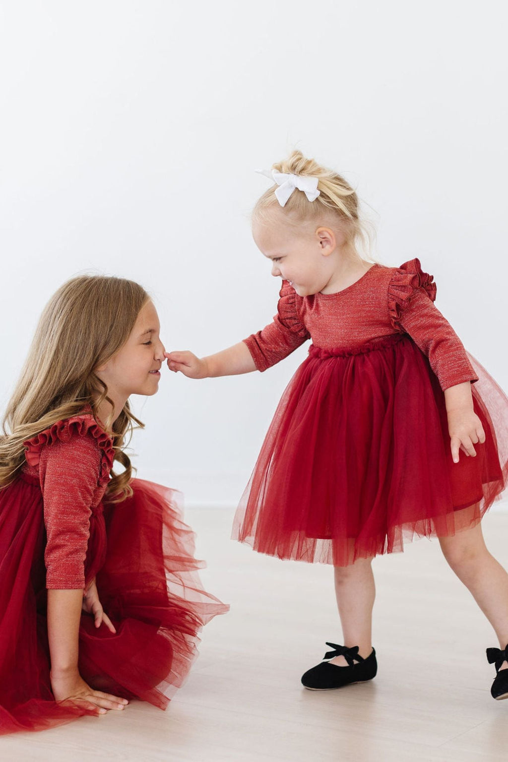 Two young girls in a Pumpkin Spice Shimmer 3/4 Sleeve Tutu Dress, one playfully touching the other's nose, showcasing the dress's vibrant color and playful design in a joyful moment.