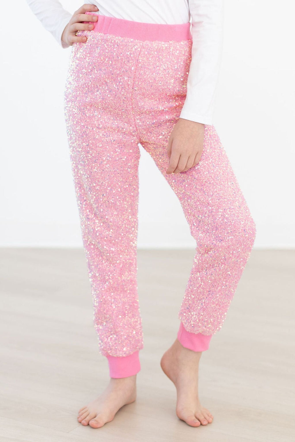 A child wearing Bubblegum Pink Sequin Joggers featuring a vibrant pink color with eye-catching sequin details. The joggers have an elastic waistband and cuffs, perfect for a chic and comfortable look.