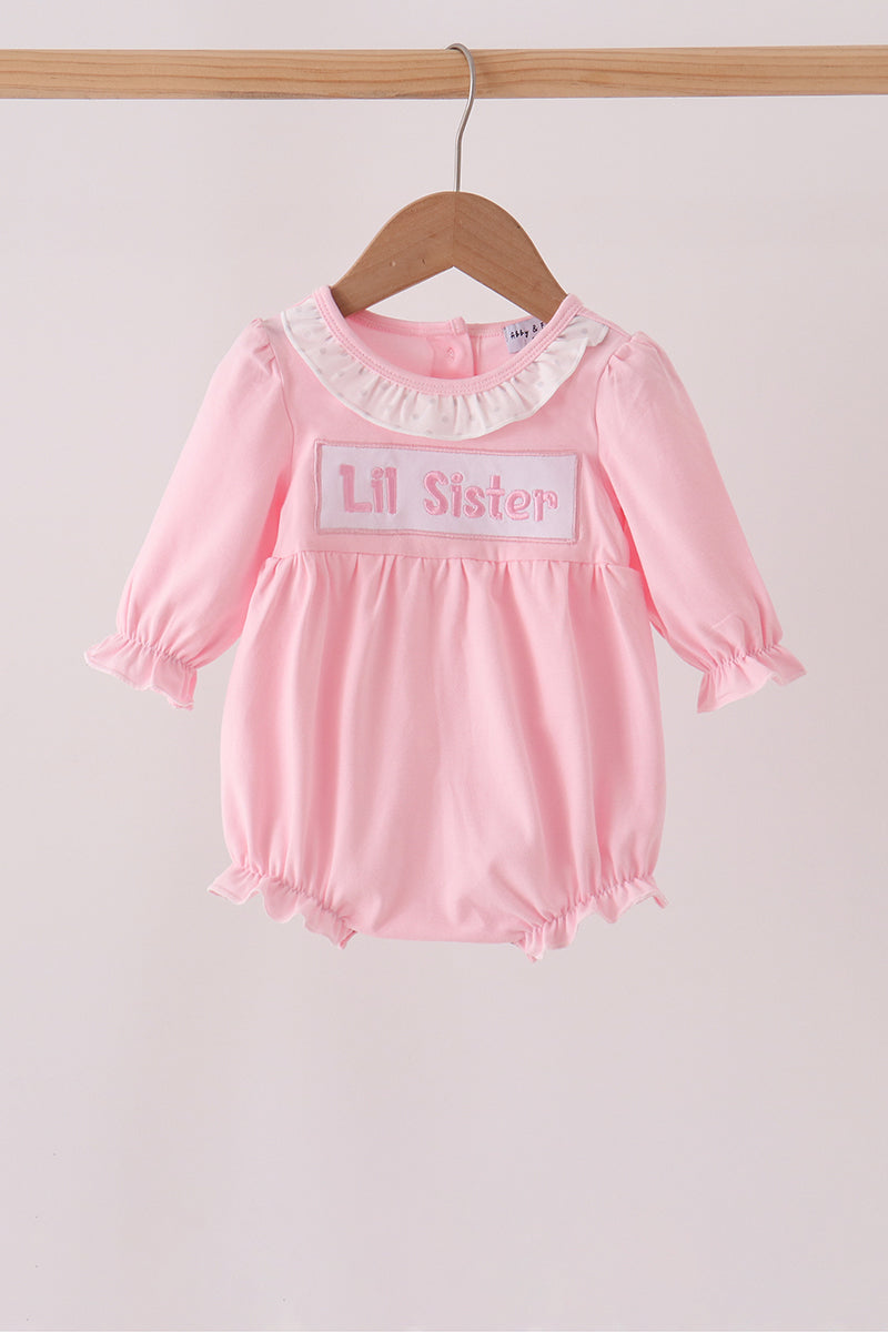 Light pink long-sleeved bubble romper on wooden hanger with white polka dot ruffle collar and 'Lil Sister' embroidery