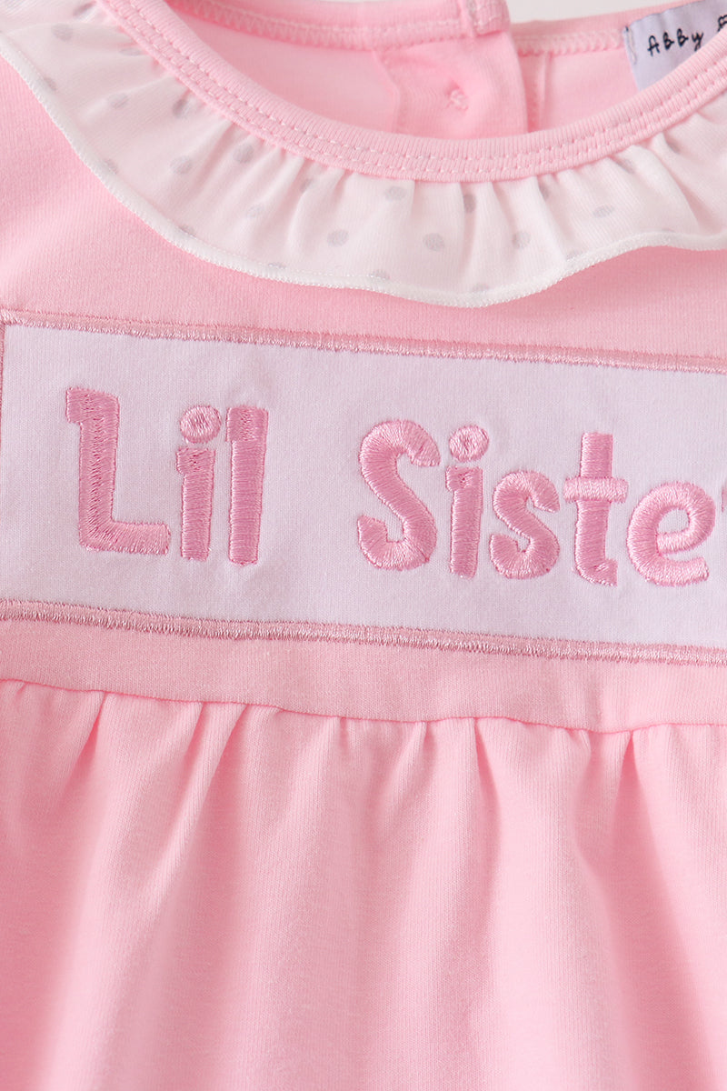 Close-up of raised 'Lil Sister' text embroidery on pale pink patch with white polka dot ruffled collar detail