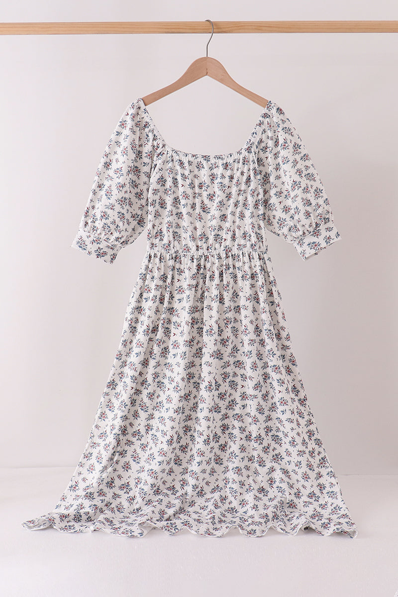 White dress with small teal and pink floral print, featuring puff sleeves, smocked bodice, and square neckline for modern mom style.