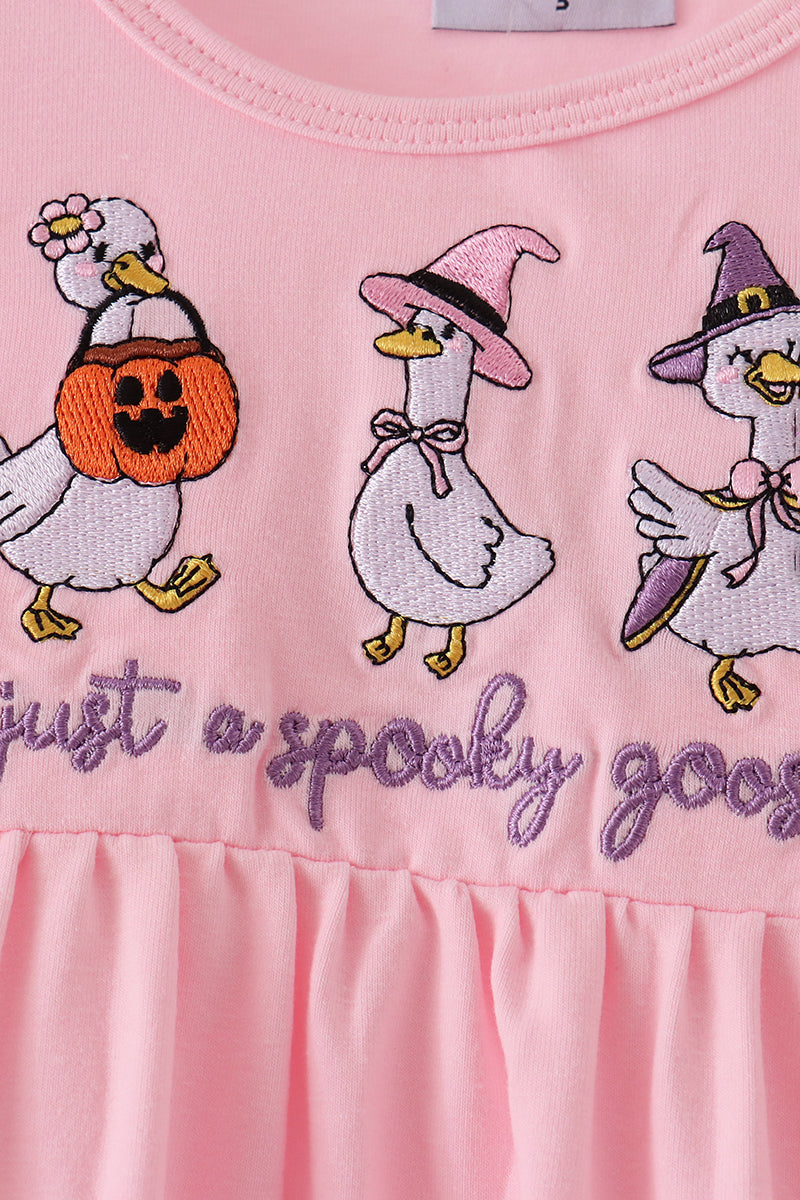 Close-up of a pink children's garment with embroidered white decorative ducks in Halloween costumes and purple script text reading 'just a spooky goos'.