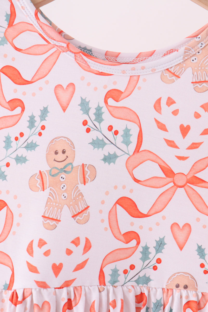 A close-up of a sleeveless top or dress featuring a festive Christmas print with gingerbread men, hearts, ribbons, candy canes, and holly on a pale pink background.