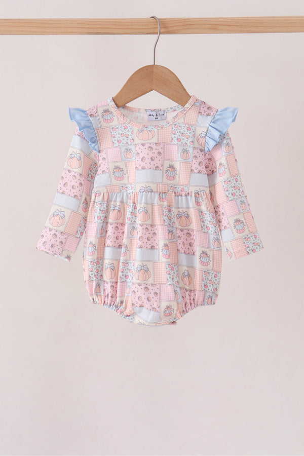 A baby girl's long-sleeve romper with a pink patchwork print featuring light blue ruffle sleeves, hanging on a wooden hanger from a light wood rod against a solid light beige background.