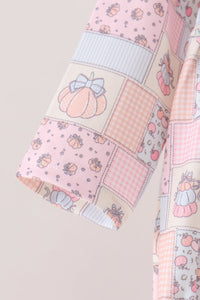 A close-up of a patchwork fabric garment, likely a robe or blanket, featuring pastel pink, peach, and light blue squares with pumpkin, gingham, and floral patterns.