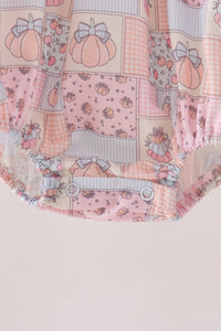 A close-up of a baby romper or bodysuit featuring a patchwork print of pink pumpkins, gingham, polka dots, and striped patterns, with ruffled snap closures at the bottom.