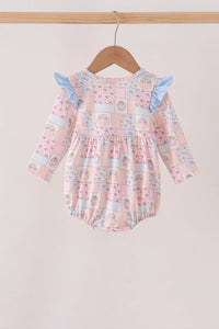 A baby girl's long-sleeve romper with a pink patchwork print, featuring light blue ruffle shoulder details, hanging on a wooden hanger against a soft beige background.