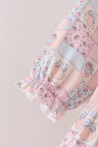 A close-up of a patchwork-patterned blouse sleeve with ruffled trim. The fabric features various pastel panels including pink gingham, peach illustrations with bows, strawberry prints, and light blue stripes, set against a solid pale pink background.