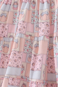 A close-up of a tiered ruffle skirt featuring a patchwork print of pink pumpkins, cherries, gingham, polka dots, and stripes on a cream background.